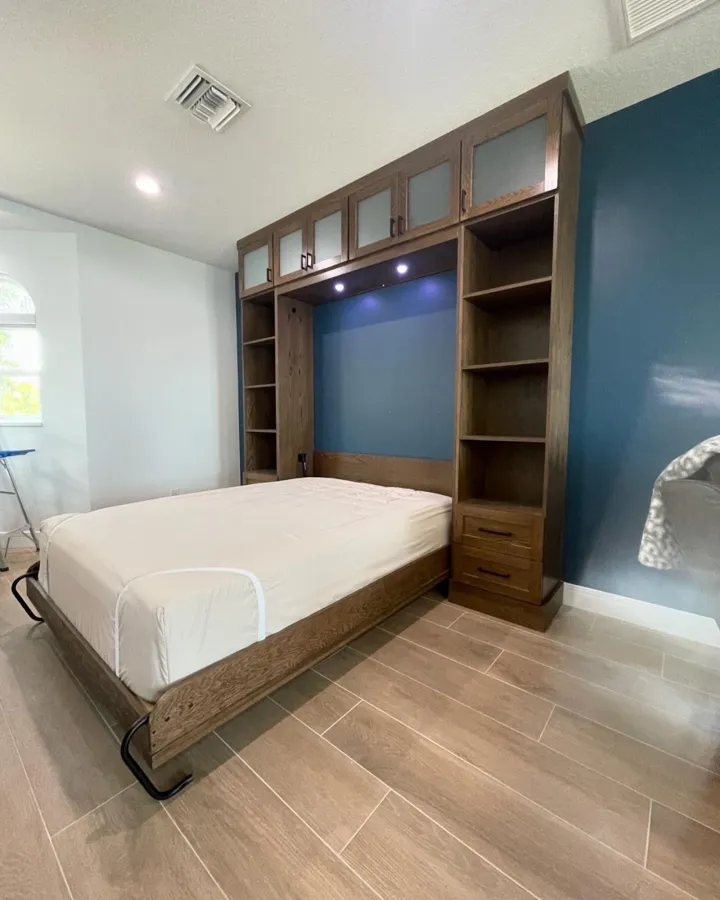 Murphy bed folded down from a wood wall unit with shelves and cabinets