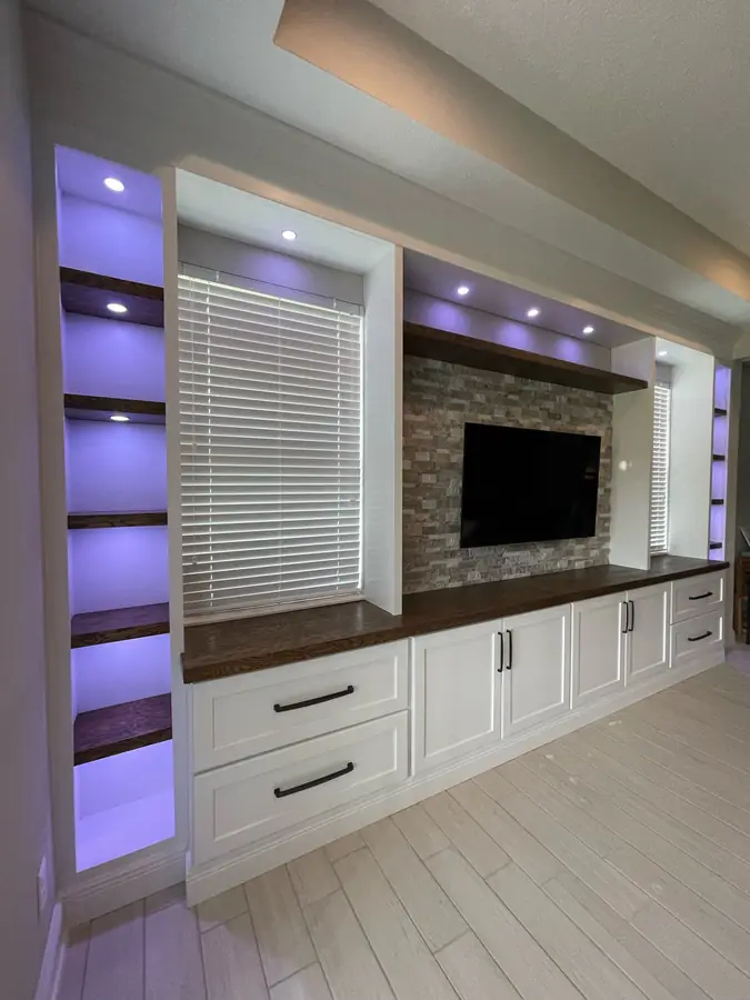 White built-in with LED-lit shelves and a stone TV wall by Frost Custom Carpentry in Tampa, FL